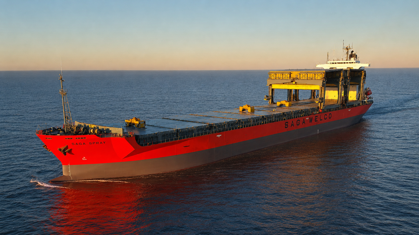 Open-hatch box-shaped general cargo vessel with deck gantry cranes under way in open water at first light.