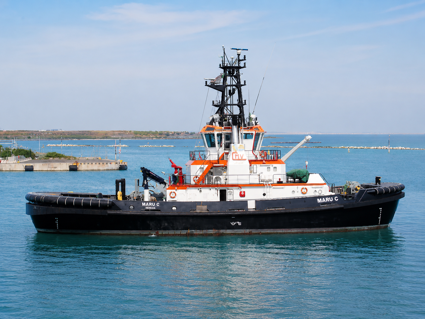 Harbour tug under way in calm blue water, black hull with white superstructure, orange trim and fendering.