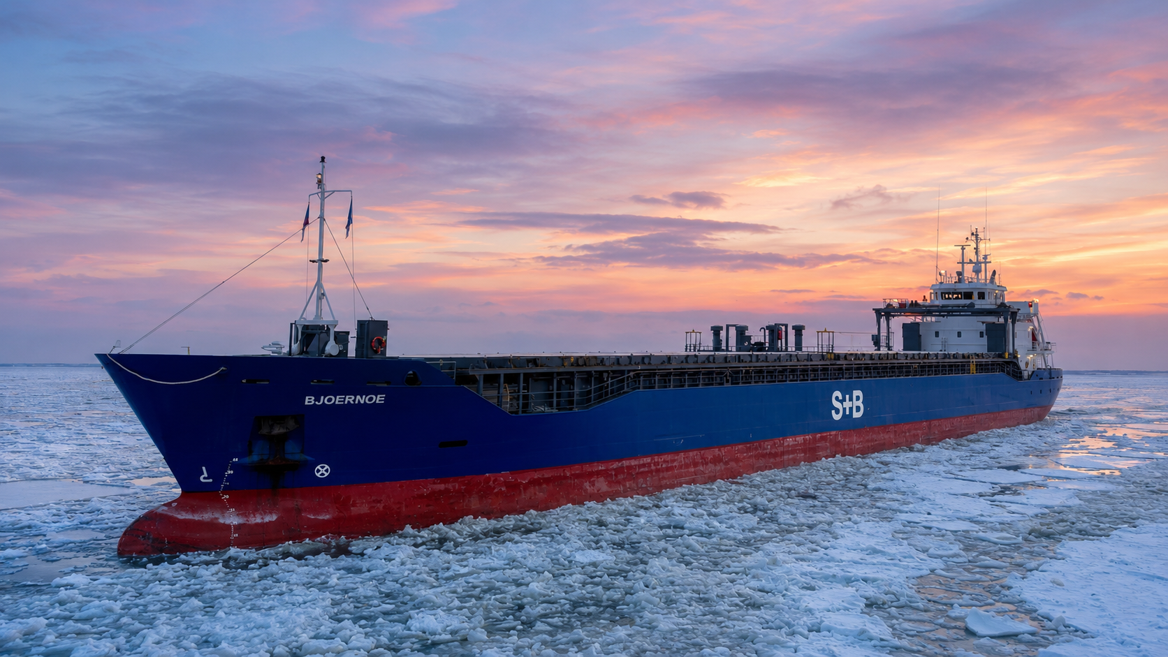 General cargo vessel BJOERNOE with a two-tone blue and red hull proceeding through broken drift ice at sunset, hatch covers closed and bow mast raised.