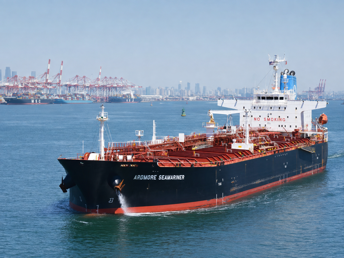 Product tanker ARDMORE SEAMARINER under way in a harbour approach, container terminal cranes and city skyline in the background.